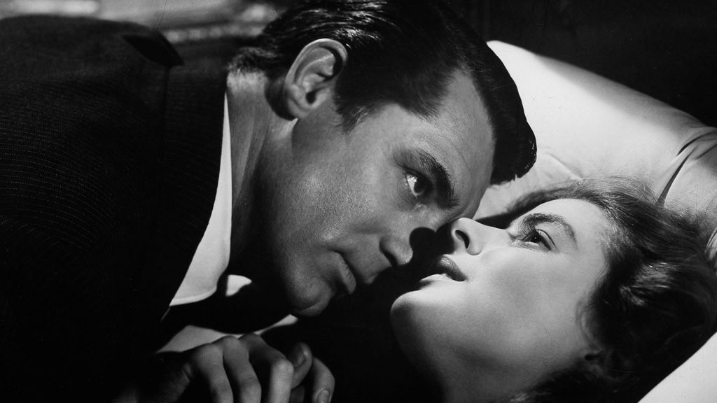 Cary Grant menacingly leans over Ingrid Bergman in bed, closer up.